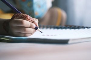 Niño escribiendo en un cuaderno pequeño artesanal con lápiz de madera