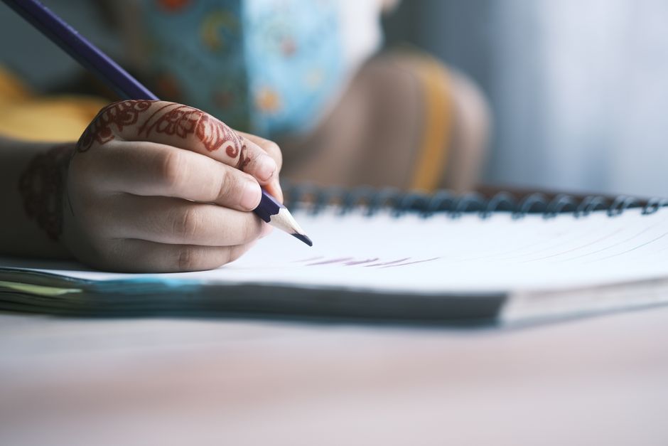 Niño escribiendo en un cuaderno pequeño artesanal con lápiz de madera