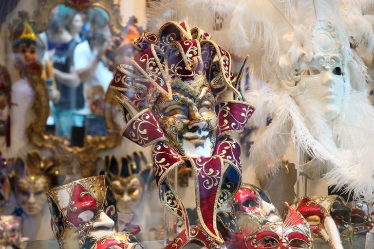 Colección de máscaras venecianas artesanales expuestas en pared con iluminación de vitrina
