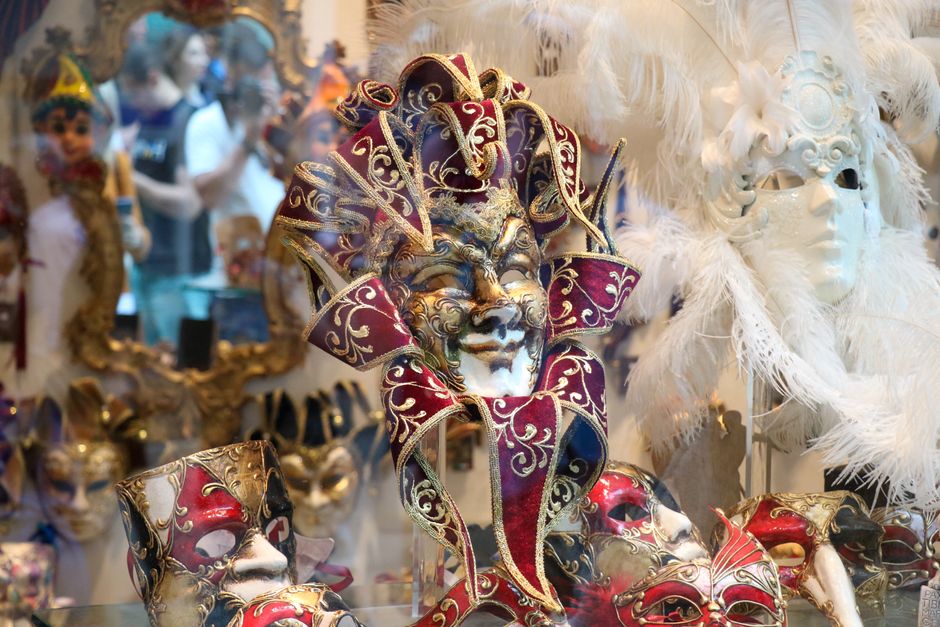 Colección de máscaras venecianas artesanales expuestas en pared con iluminación de vitrina